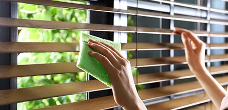 A person dusting wooden window blinds with a cloth.
