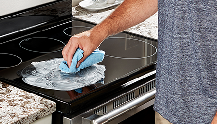 Une personne applique un nettoyant pour table de cuisson sur une table de cuisson en verre.
