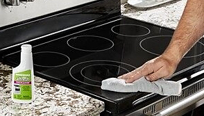 Someone wipes clean an induction cooktop with a light blue dish cloth