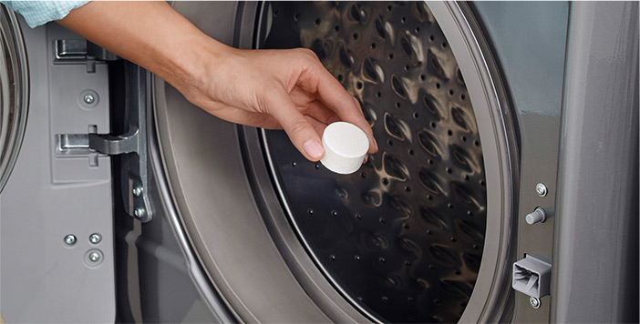 Someone holds an affresh tablet at the opening of a washing machine