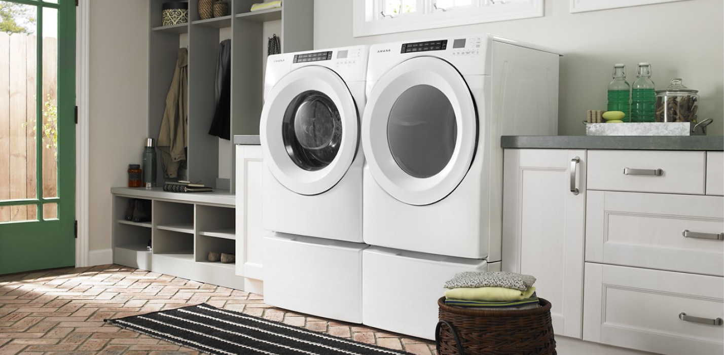 A white Amana® front load washer and dryer set in a bright laundry room with white cabinets