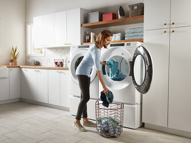 Woman loading laundry into a white washer and dryer