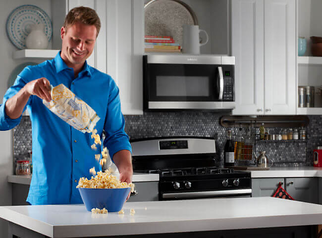 Person pouring popcorn into bowl in kitchen with Amana® range and microwave