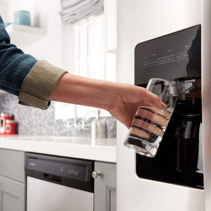 Person filling a glass from a refrigerator water dispenser Person filling a glass from a refrigerator water dispenser