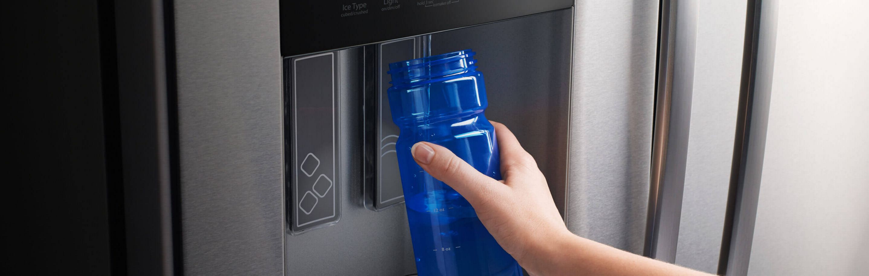 Person filling a water bottle from a refrigerator water dispenser
