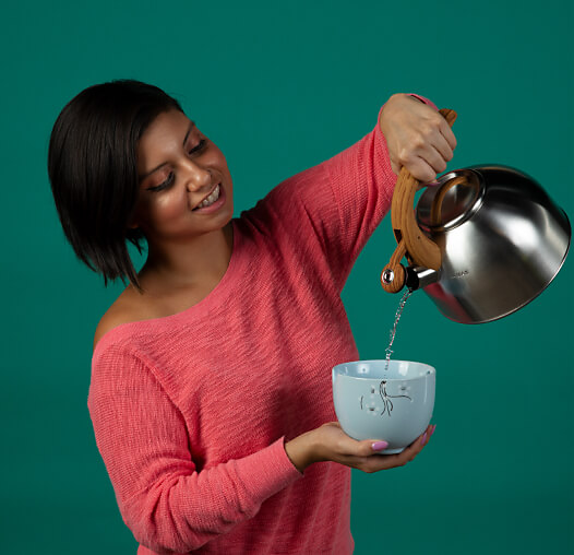 A woman pouring water from a kettle into a bowl.