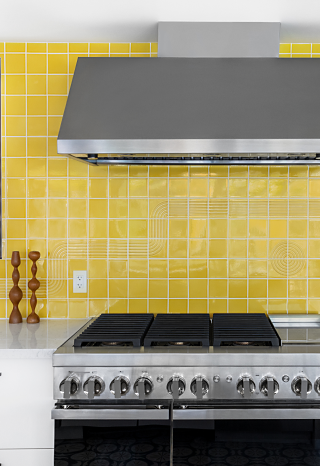 A JennAir® NOIR™ Professional Range and Commercial Hood in a kitchen with a yellow backsplash.