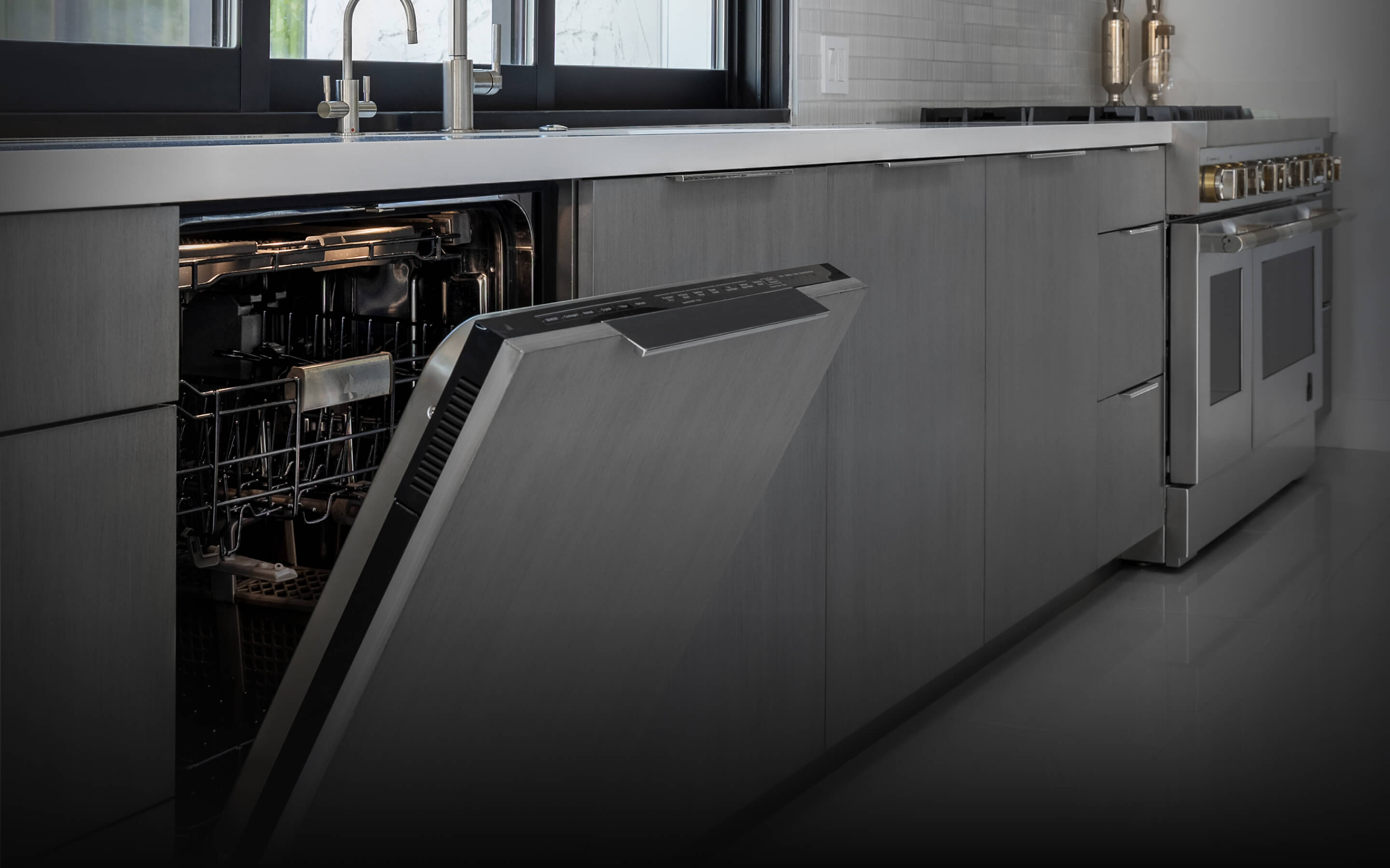 A JennAir® Panel-Ready Dishwasher with its door slightly ajar in a kitchen with gray cabinets.