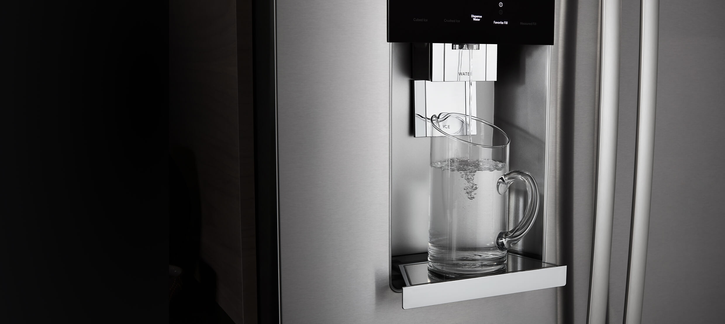  The front of a JennAir® built-in refrigerator, showing water being poured into a glass from the external dispenser.