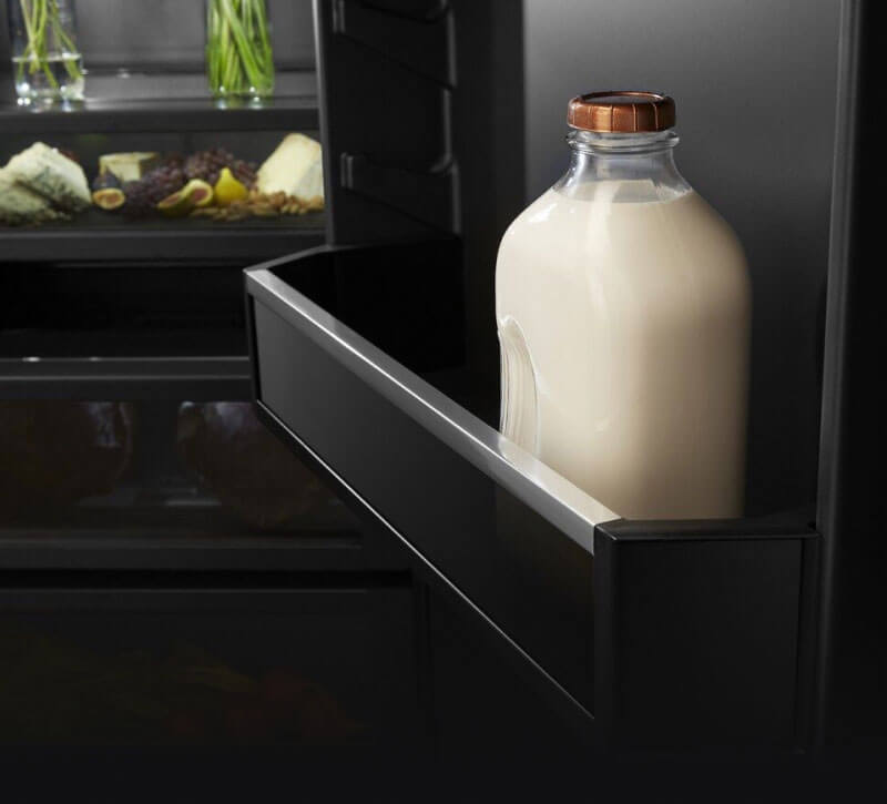 The door of a built-in refrigerator holding a glass gallon jug of milk.
