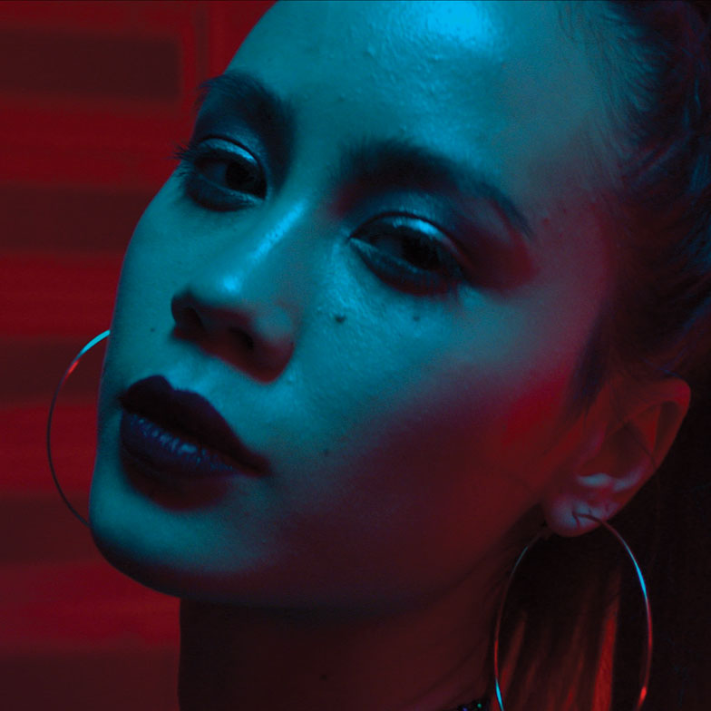 A defiant woman looking into the camera, with blue lights on her face and red lights illuminating the background. 