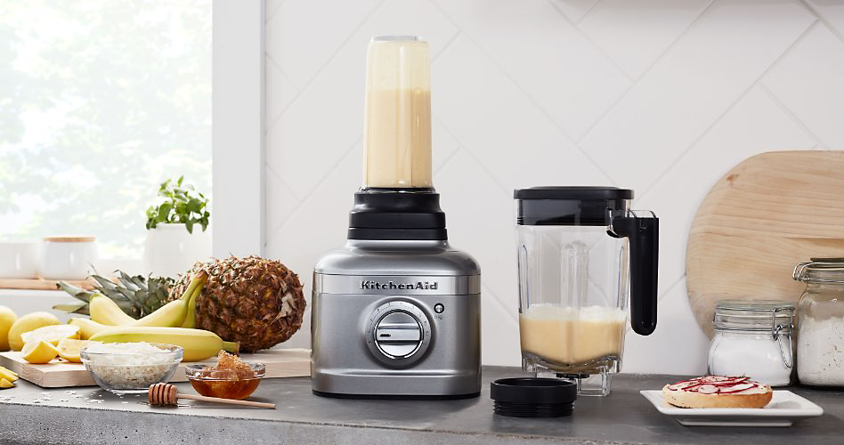 A gray Kitchenaid blender with an individual blender pitcher. On the counter: various fruits