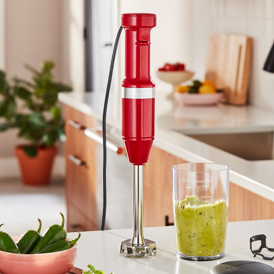 A red KitchenAid electric hand blender next to a glass containing a green smoothie