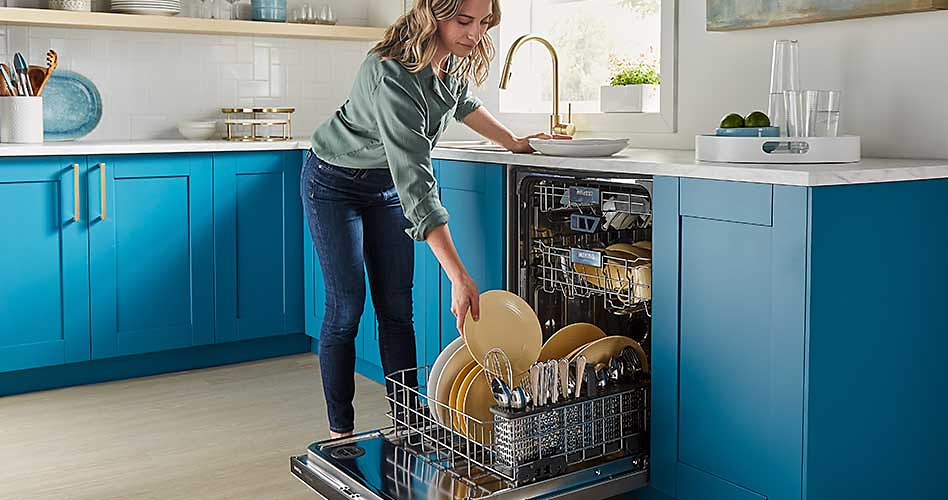 Une femme remplit un lave-vaisselle avec divers articles dans une cuisine aux comptoirs bleus