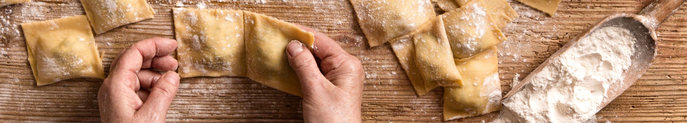 Quelqu'un fait des raviolis maison sur un comptoir couvert de farine. On y retrouve une cuillère remplie de farine
