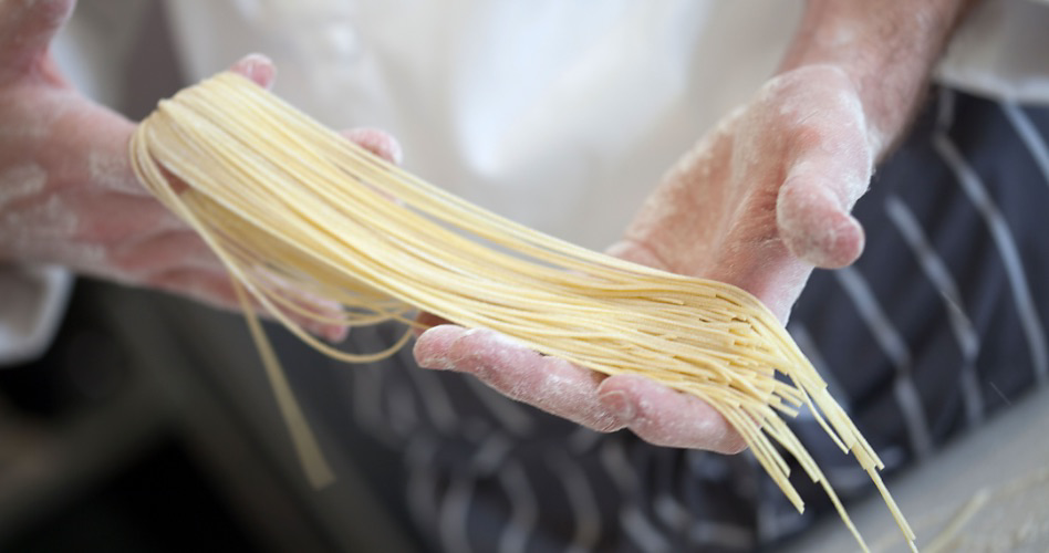 Mains couvertes de farine tenant des brins de pâtes fraîches