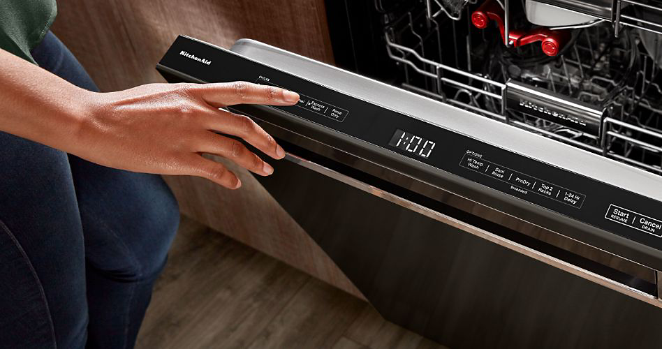 Quelqu'un sur le point d'appuyer sur un bouton de lave-vaisselle KitchenAid à commande par le haut