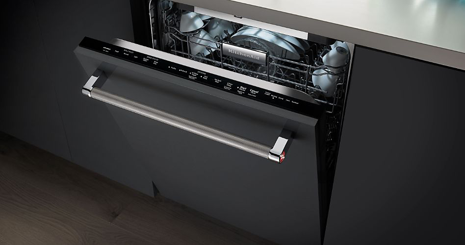 Un lave-vaisselle KitchenAid à commande par le haut avec la porte légèrement entrouverte. Sur le panier supérieur se trouvent des tasses et des bols