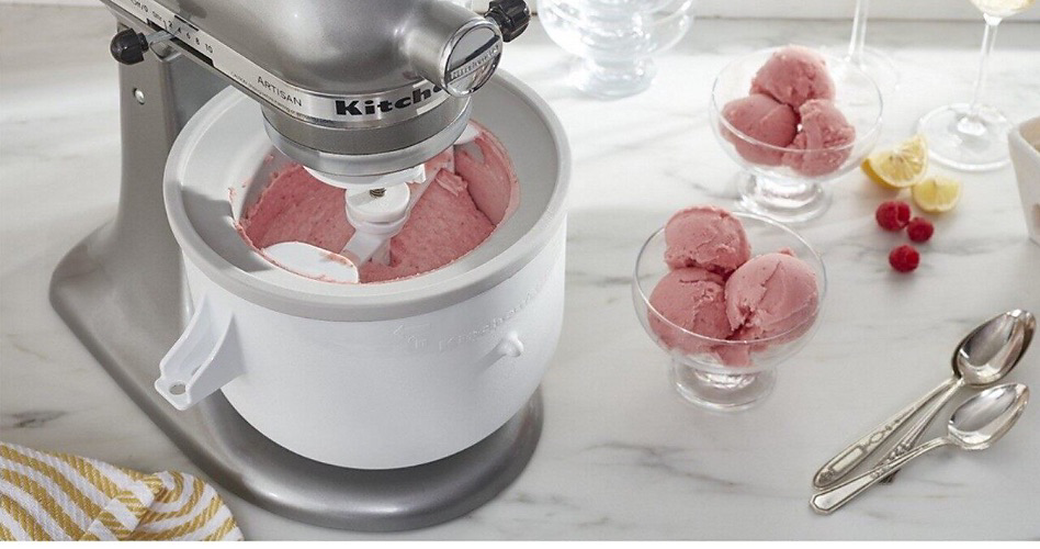 A KitchenAid Stand Mixer with an Ice Cream Attachment churning ice cream. On the counter are bowls of ice cream and two spoons