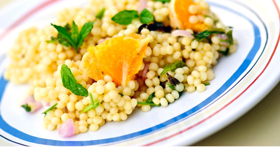 Un bol de couscous perlé avec des oignons hachés, des herbes fraîches et des morceaux d'orange
