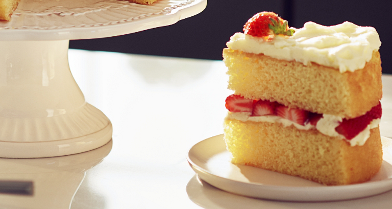 Un morceau de gâteau avec un glaçage blanc, un plateau à gâteau et des fraises sur une assiette sur un comptoir. 