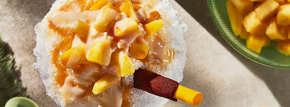 De la glace pilée garnie d'ananas avec une paille qui dépasse. À côté, un bol d'ananas coupé en morceaux.