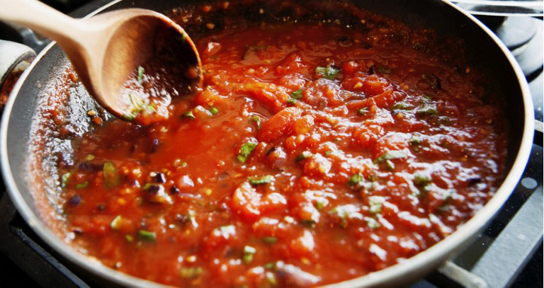 Une sauce tomate est remuée pendant la cuisson dans une casserole.