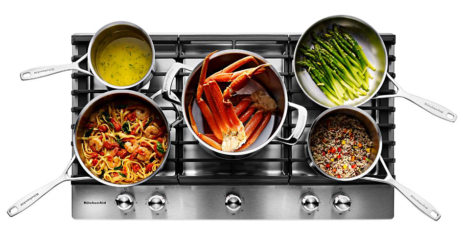 Divers aliments cuisant sur une cuisinière en vitrocéramique, comme des pattes de crabe, des asperges, des pâtes, et plus.