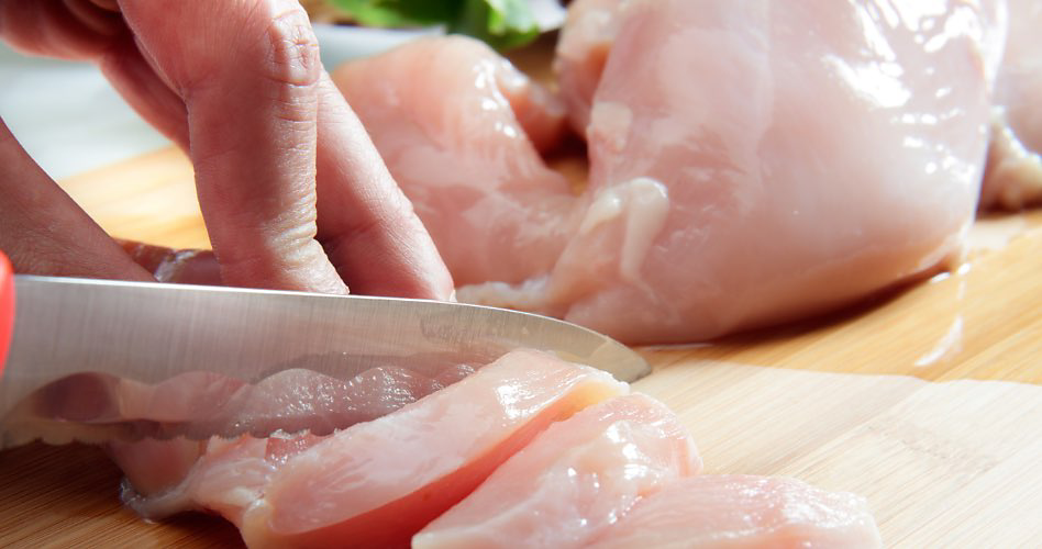 Quelqu'un qui coupe du poulet cru sur une planche à découper