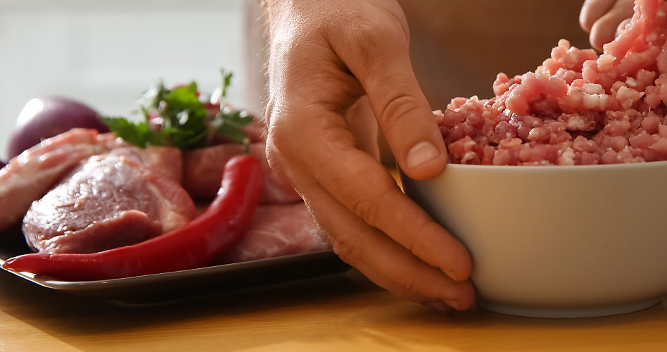 Une main touche un bol de viande hachée. À côté du bol, une assiette avec du poulet et un piment rouge