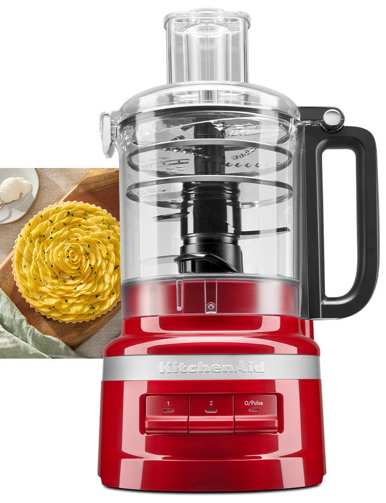 Front: KitchenAid Food Processor in Red. Background: half an avocado, half an orange, a peach and a meal in a bowl containing sliced avocado, orange wedges, brown rice, broccoli, purple cabbage