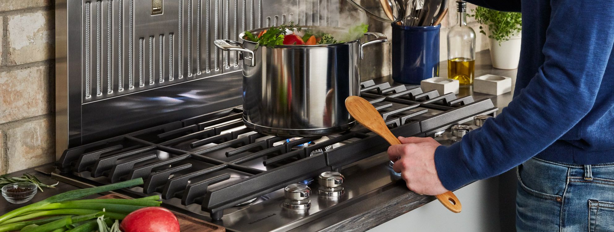 Man holding wooden spoon, boiling a pot of produce on a KitchenAid cooktop.