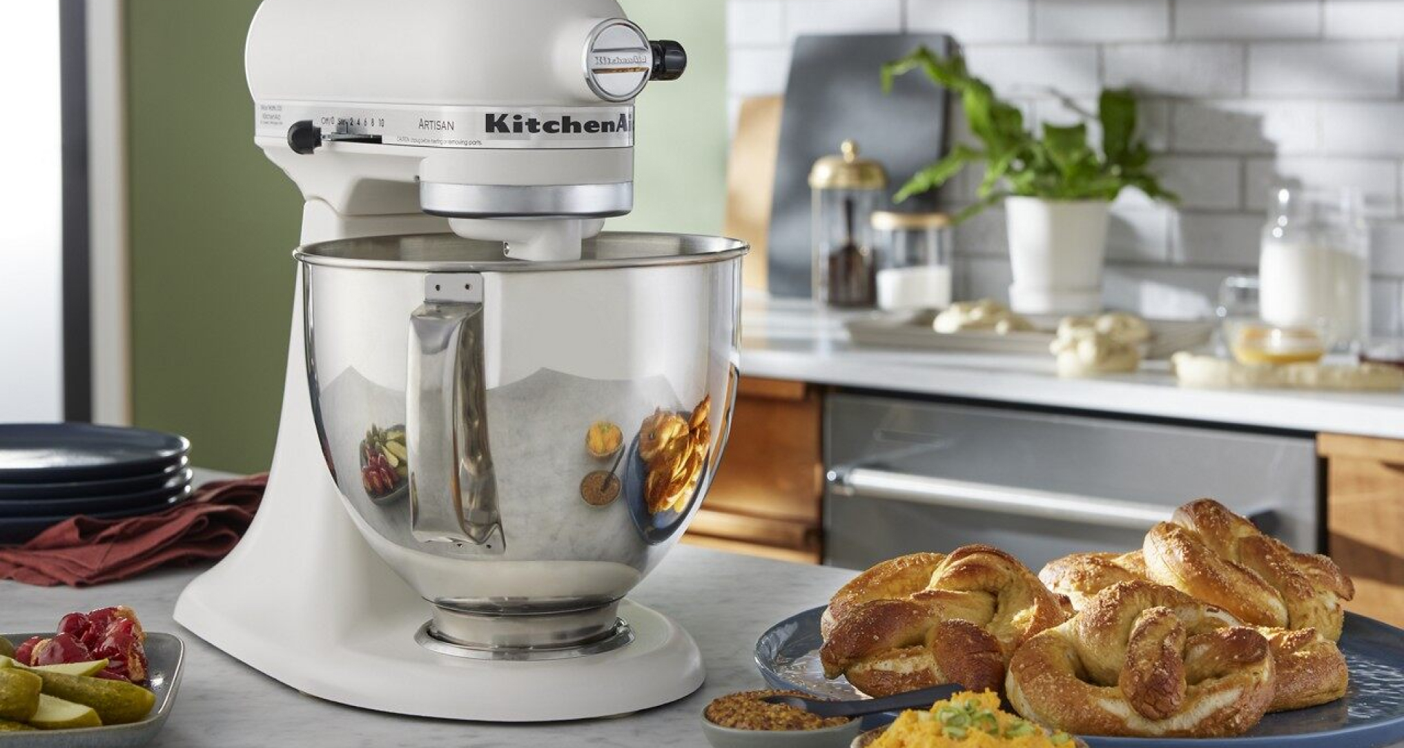 A KitchenAid® Porcelain White Stand Mixer on a countertop next to prepared braided bread.