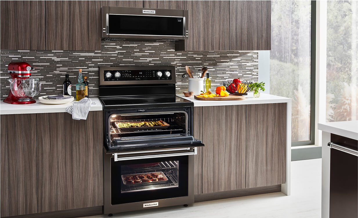 A KitchenAid® Double Oven Range in a sleek modern kitchen with wood cabinets and white countertops.
