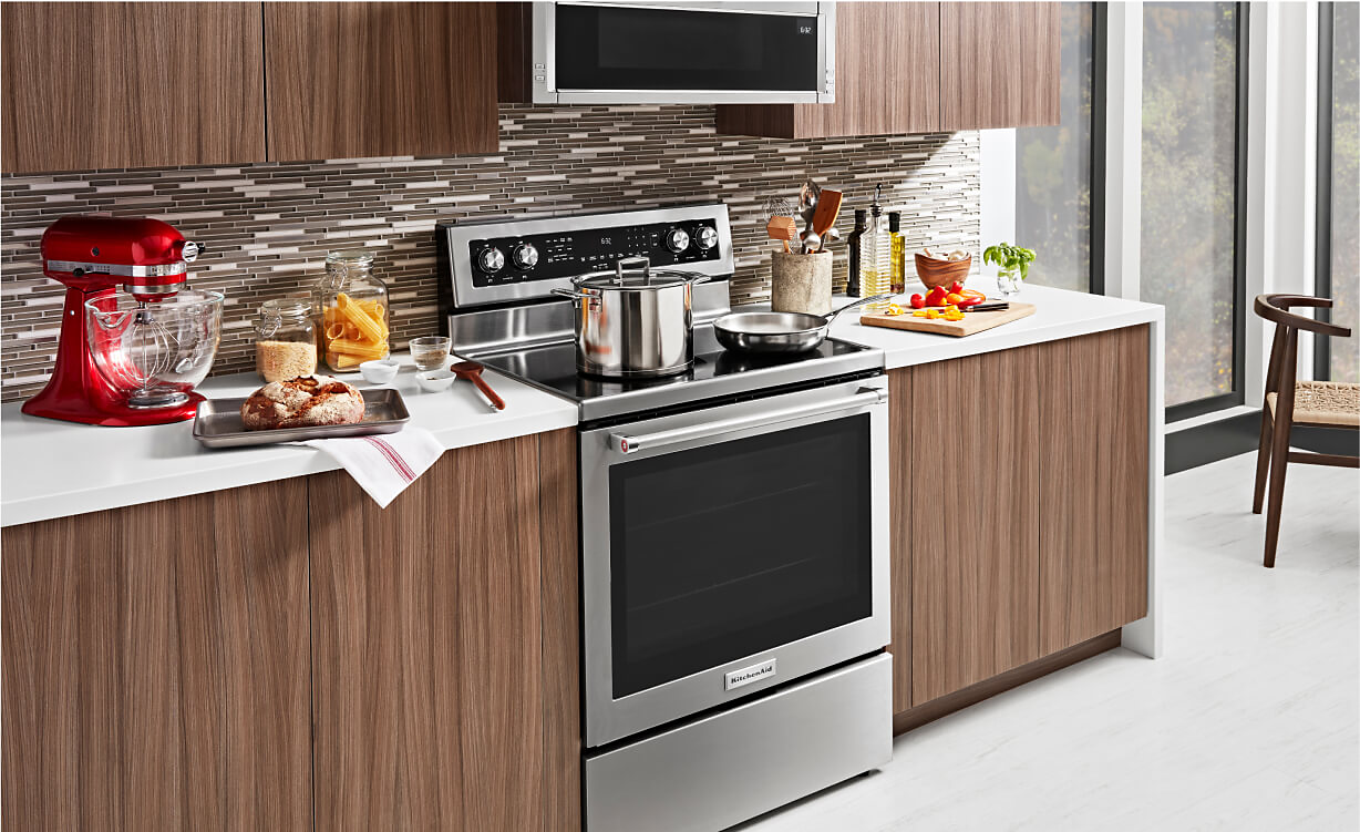 A KitchenAid® Freestanding Range in a modern kitchen with sleek wood appliances and white countertops.