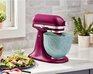 A KitchenAid® Stand Mixer in Beetroot on a countertop with a Spring Leaves bowl next to a prepared salad.