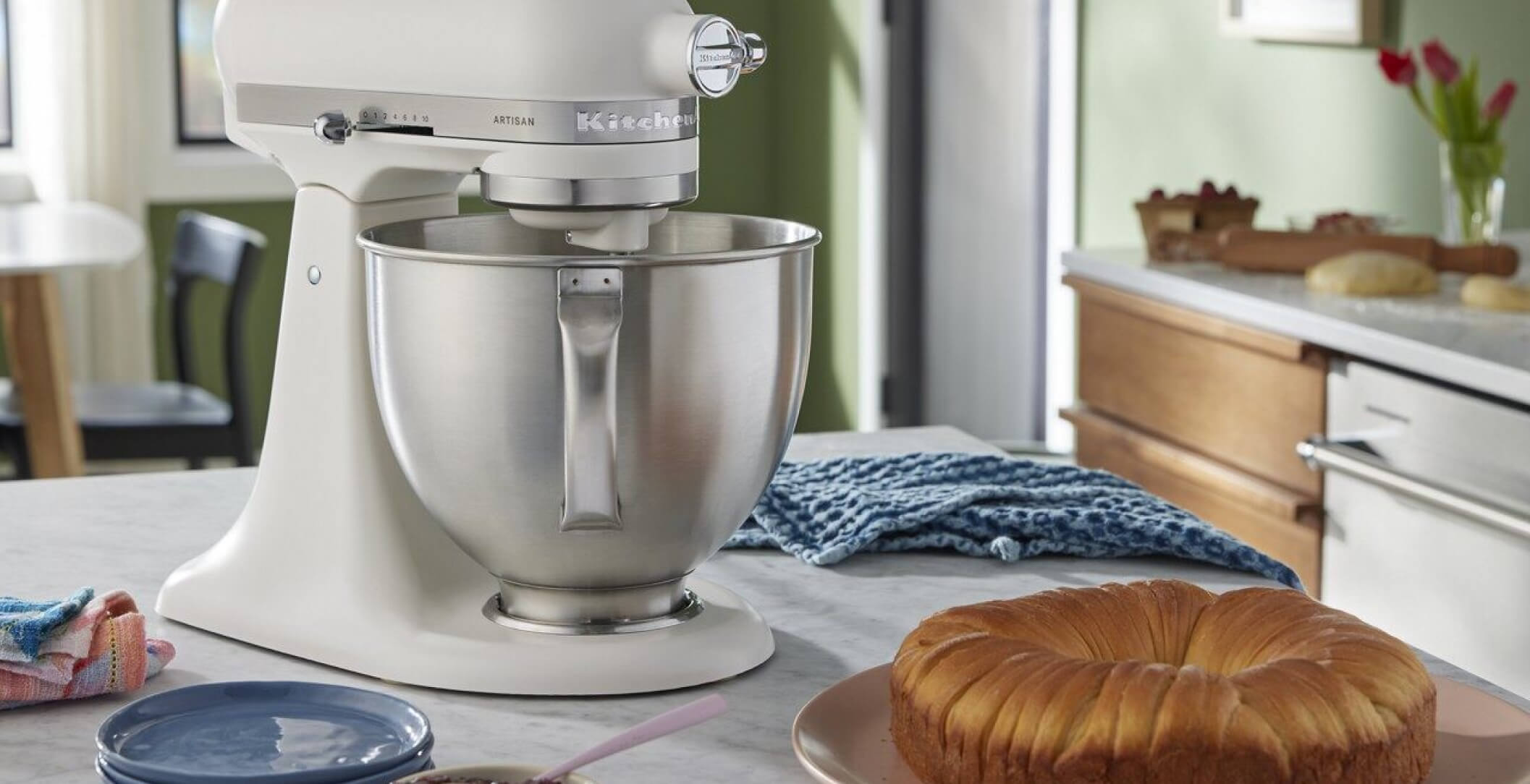 A Porcelain White Tilt-Head Stand Mixer on a countertop near a baked pastry ring.