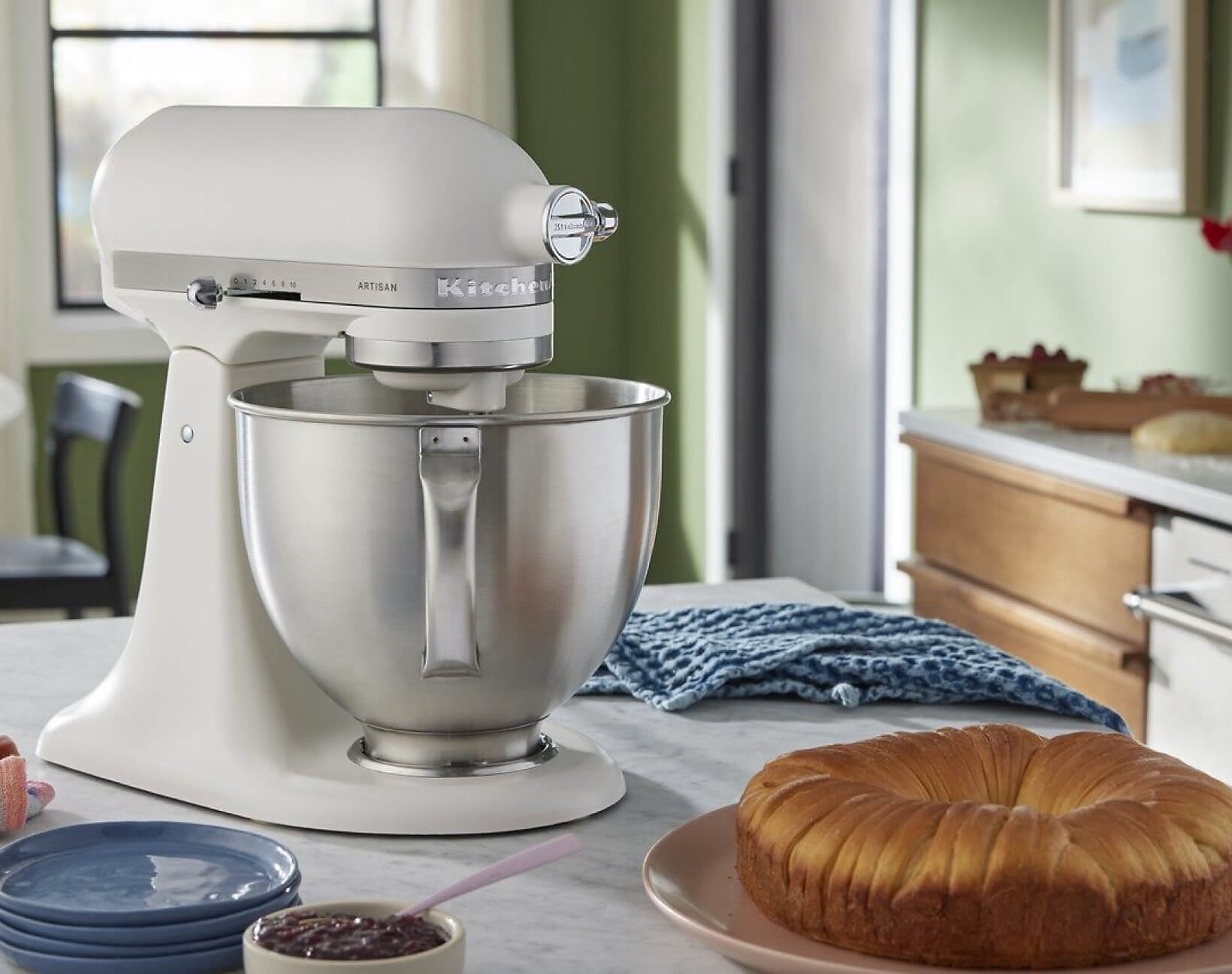 A Porcelain White Tilt-Head Stand Mixer on a countertop near a baked pastry ring.