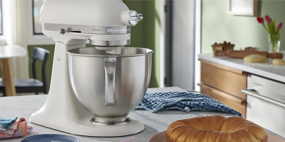A KitchenAid® Porcelain White Stand Mixer on a countertop next to a prepared pastry ring.