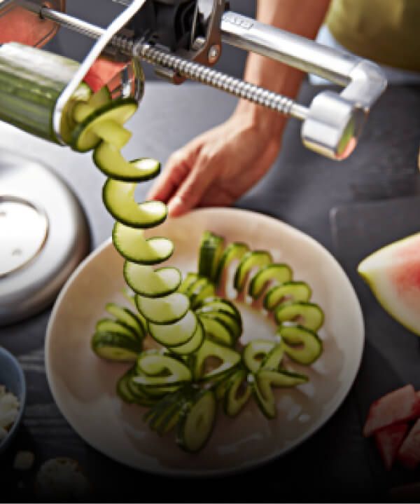 A KitchenAid® Stand Mixer using the spiralizer attachment to create zucchini spirals.