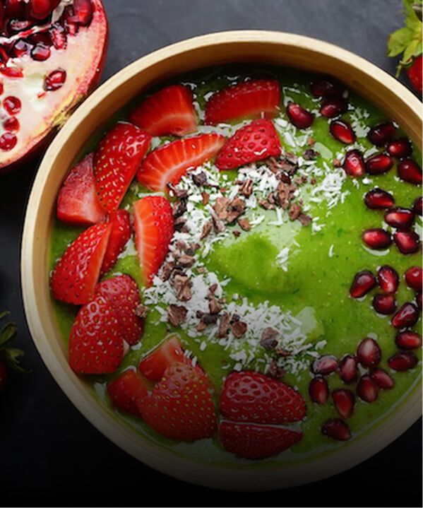 A green smoothie bowl garnished with fresh strawberries, coconut and pomegranate.