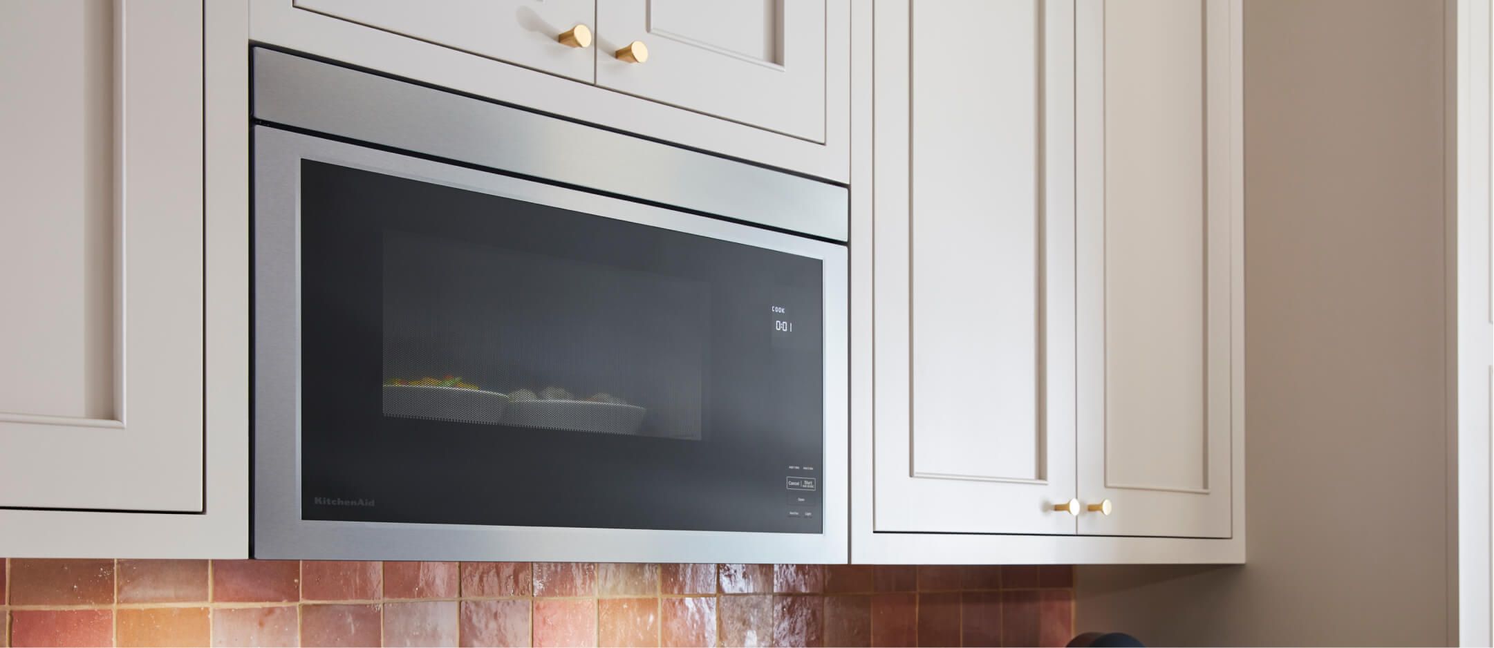 A flush KitchenAid® microwave installed over a range in line with cabinets. 