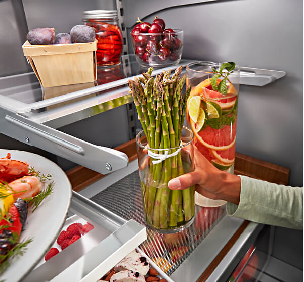A person placing asparagus in a jar with water into a KitchenAid® refrigerator.