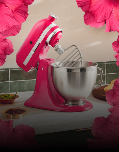 A KitchenAi® Stand Mixer in Hibiscus, with fuschia petals at the edges of the image.