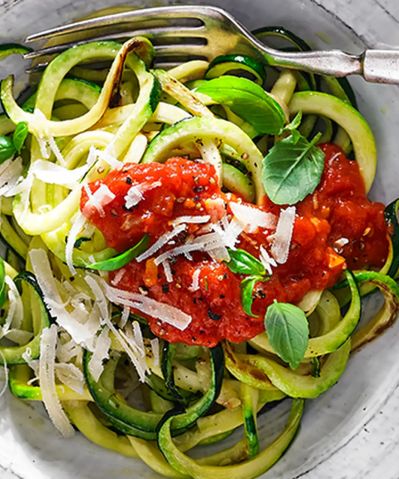 A bowl of zucchini pasta garnished with cheese and basil.