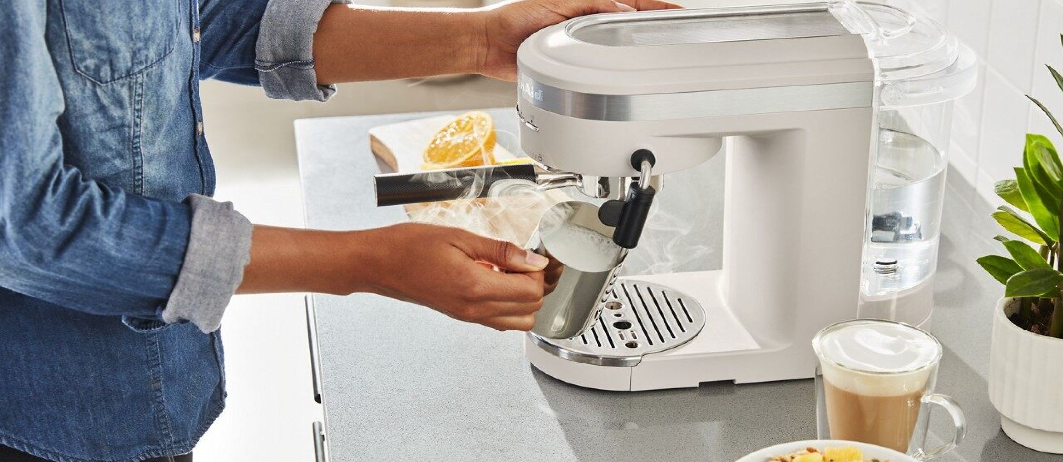 A person brewing espresso in a KitchenAid® espresso machine on a countertop.