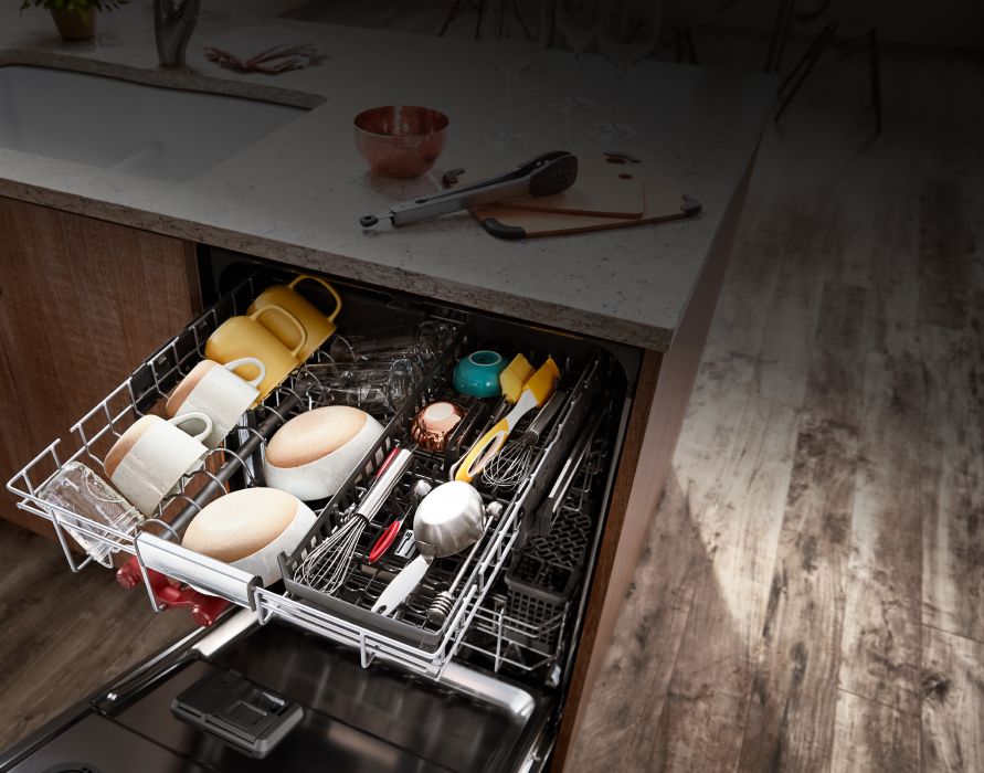 A top-down view of the fully loaded top rack in the KitchenAid 3rd Level Rack Dishwasher — with bowls, mugs and large cooking utensils laying in neatly organized rows.