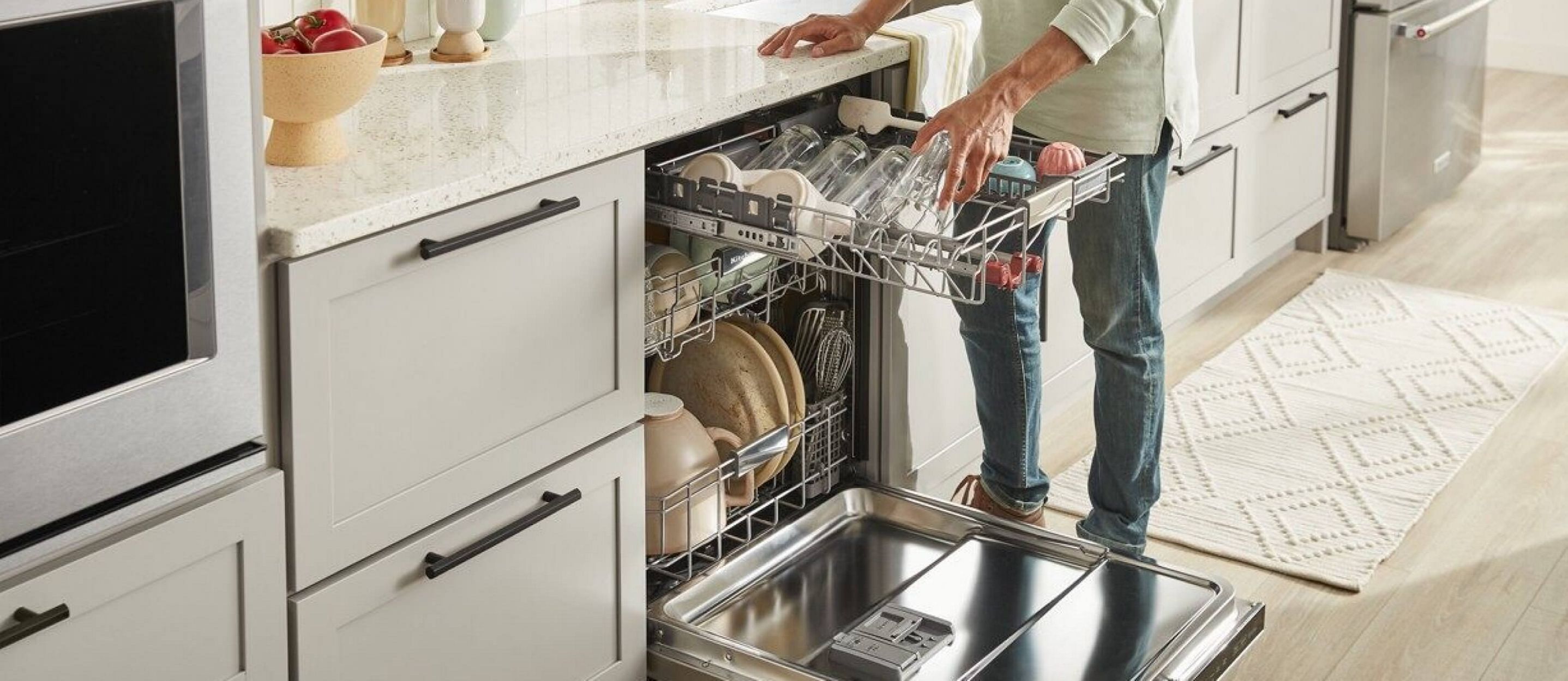 A person placing cups and glasses into the third rack of a KitchenAid® dishwasher.