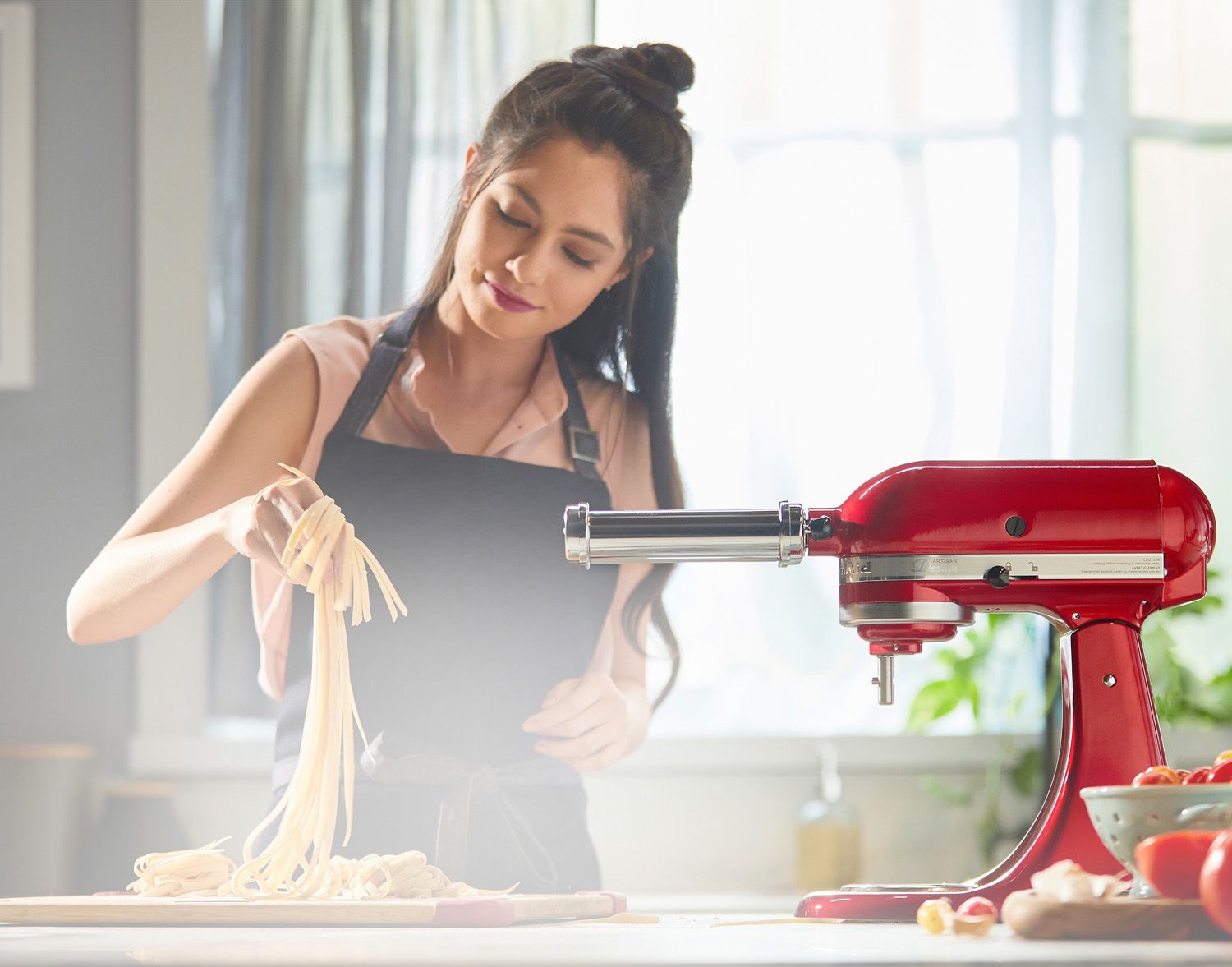 Una mujer haciendo pasta en su cocina con el aditamento de rodillo de pasta de su batidora KitchenAid.