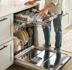 A person loading dishes onto a 3rd level rack.